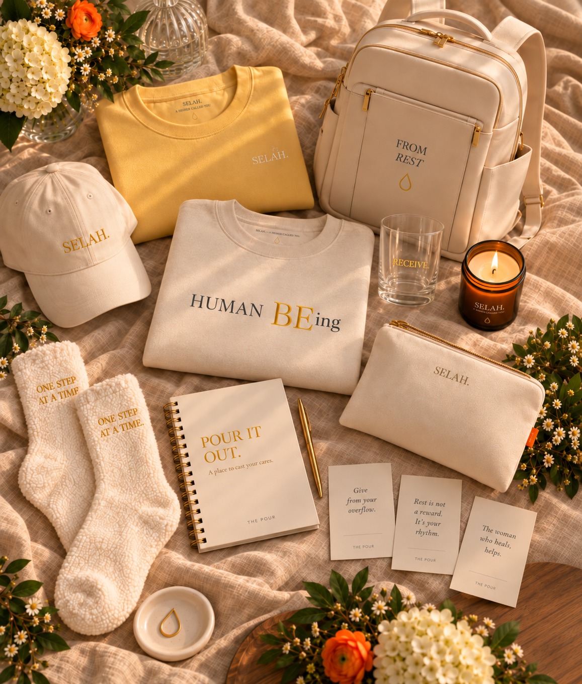 The Pour Collection preview with golden SELAH apparel, HUMAN BEing sweatshirt, bag, journal, slippers, glass, candle, and reflection cards